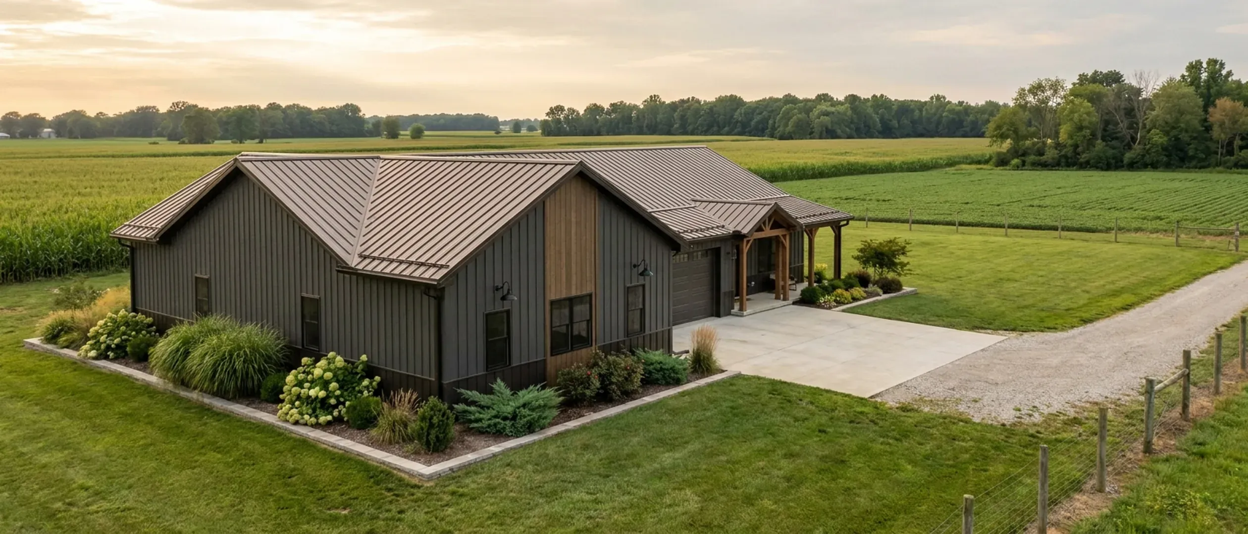 A completed barndominium viewed from a low angle showing its standing seam metal roof, vertical wall panels, gutters and exterior wall lights.