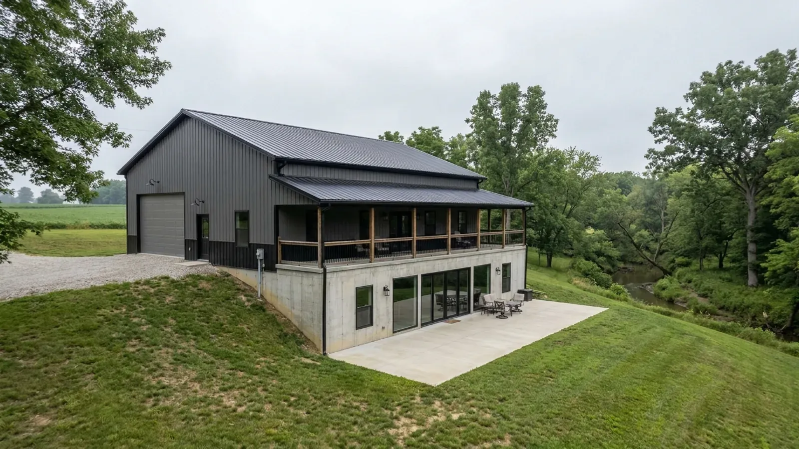 A barndominium with a walkout basement built into a sloping lot, the lower level opening onto a patio at grade.