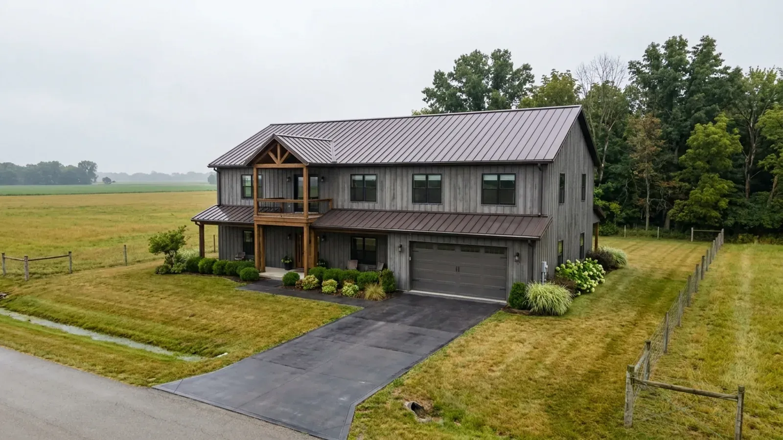 A completed two-story barndominium with visible second-story windows and a small covered balcony above the entry porch.